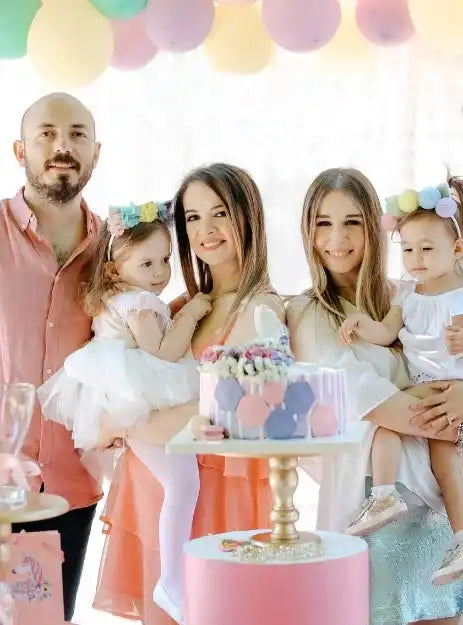A family celebrating a birthday with colorful balloons and two cakes.
