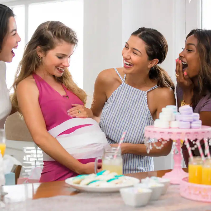 Four women at a baby shower, one with a measuring tape around her pregnant belly.