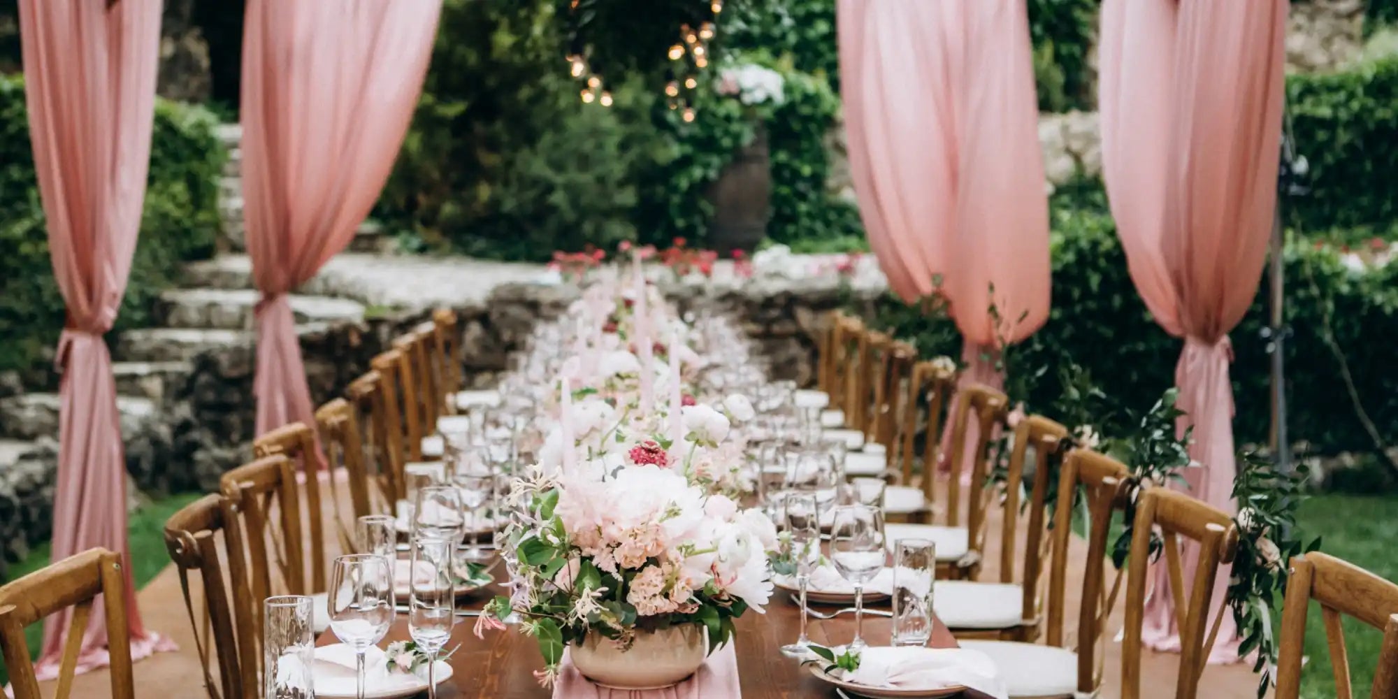 An outdoor wedding reception table set with floral arrangements and place settings.