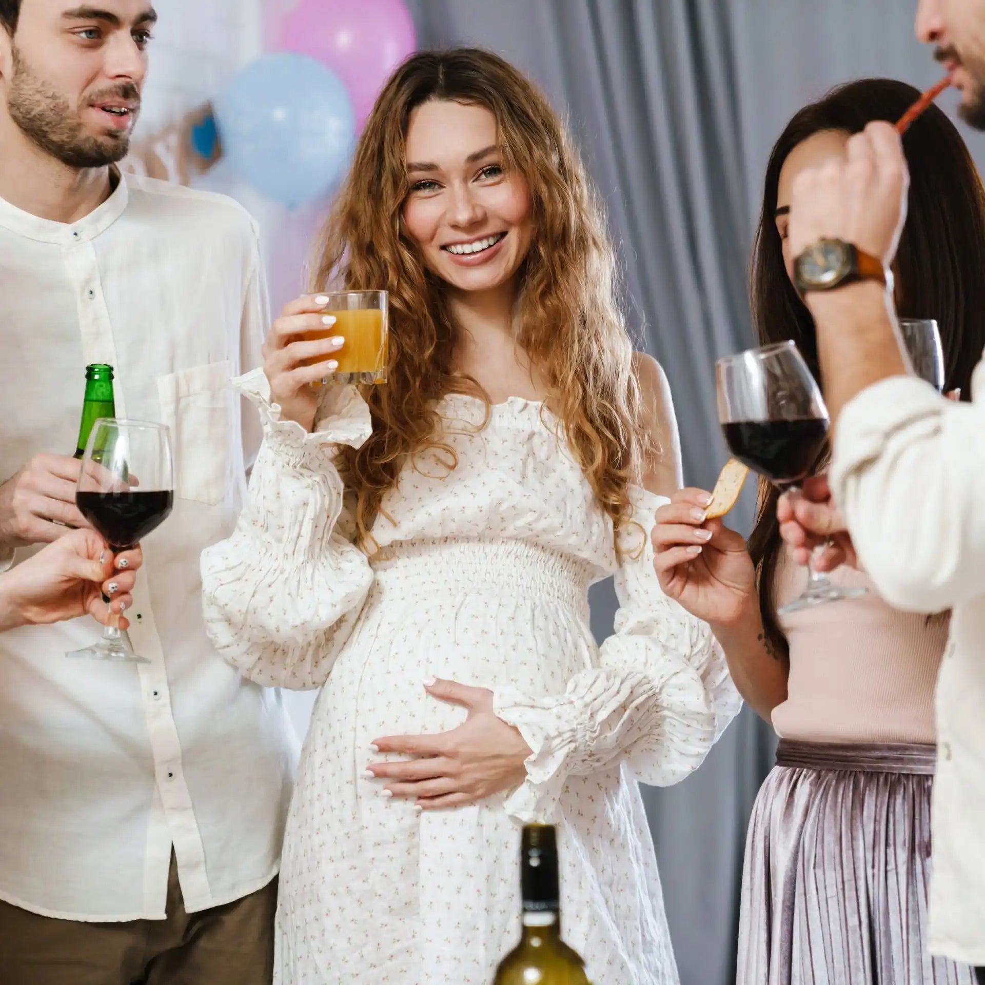 A pregnant woman in a white dress holding a drink at a celebration.