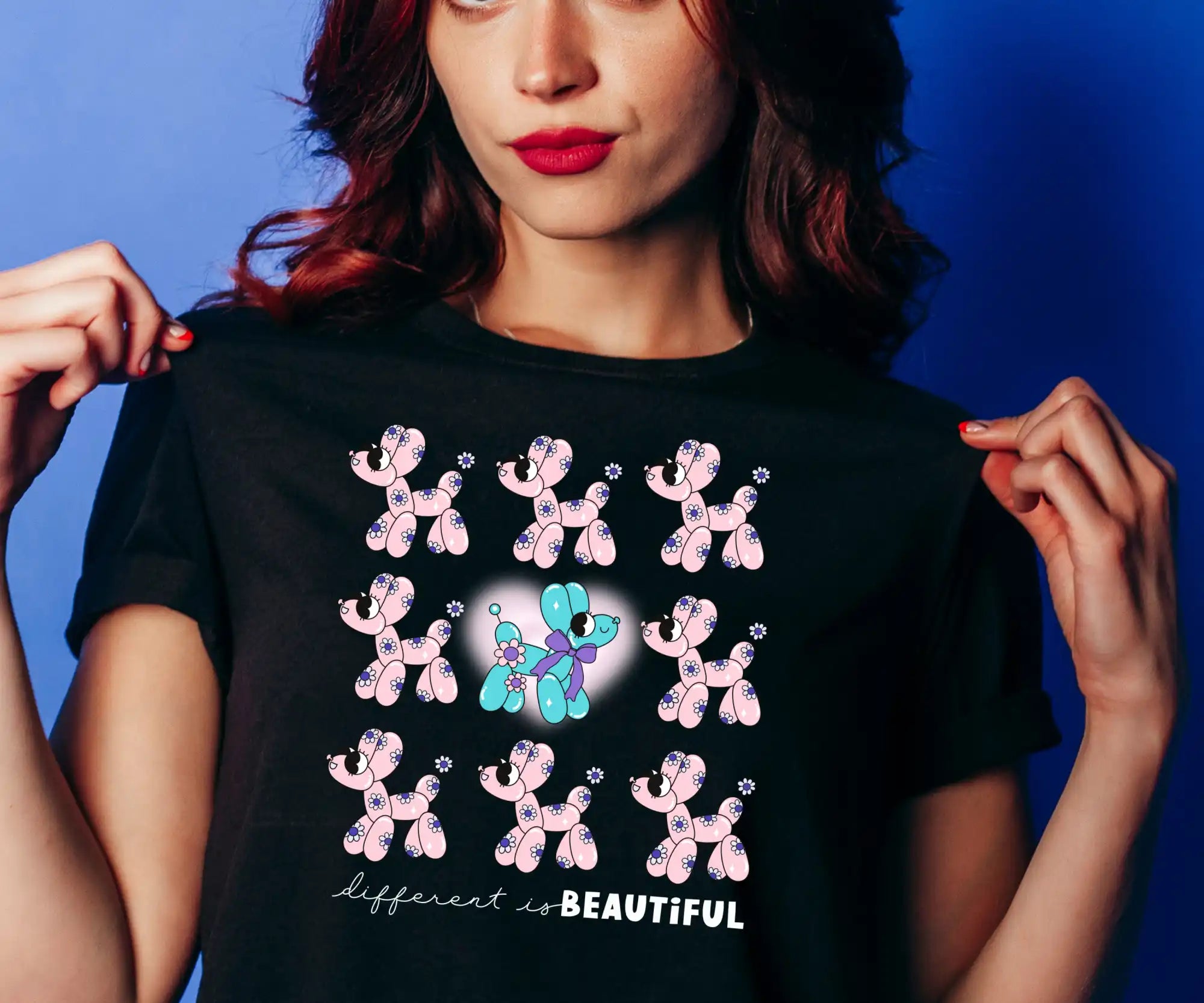 A black t-shirt featuring nine balloon poodles, one of which is blue and purple with a heart behind it, and the text ’different is BEAUTIFUL’ below.