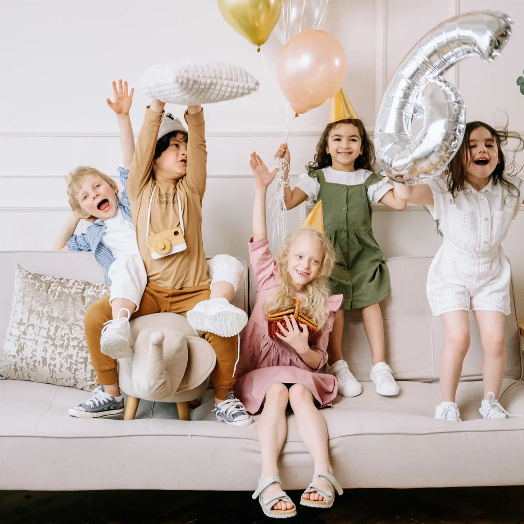 Children celebrating with balloons and party decorations on a couch