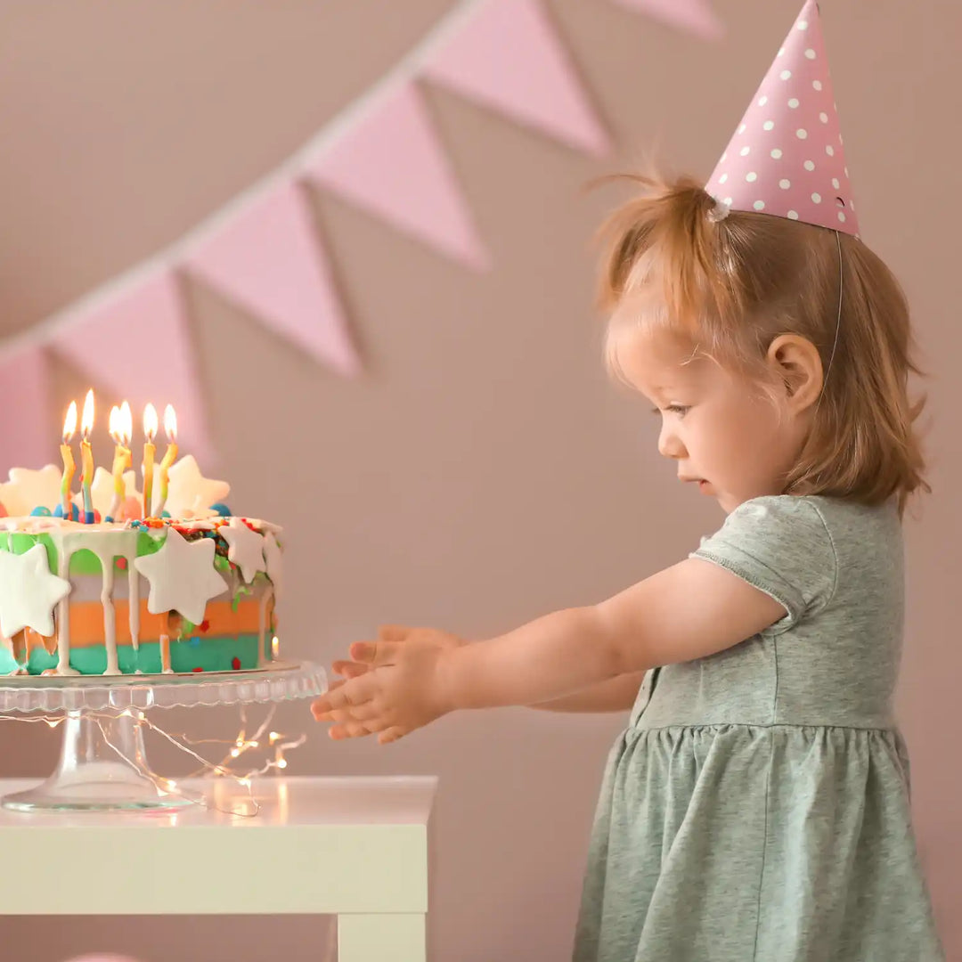 Colorful birthday cake with lit candles and green frosting drips on a cake stand