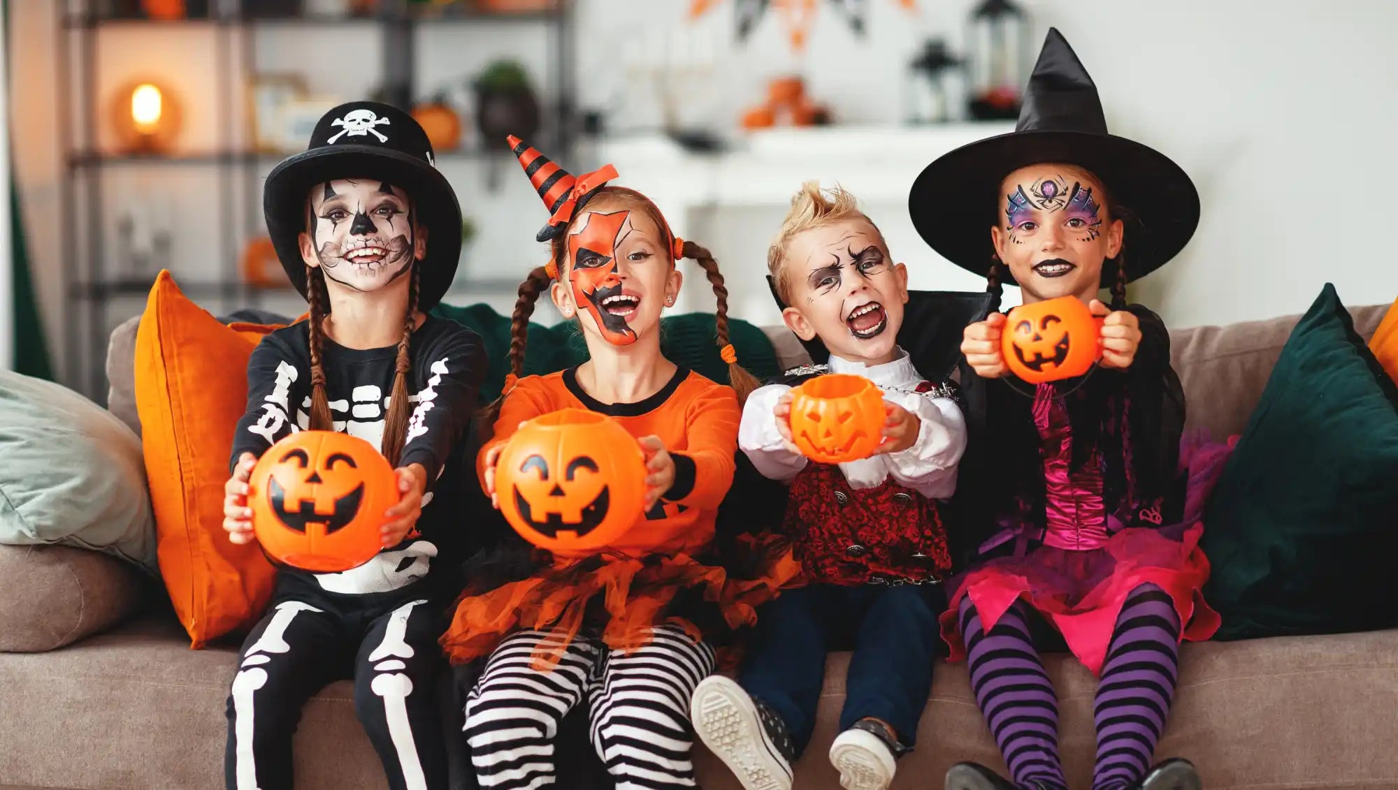 Four children in Halloween costumes holding pumpkin candy buckets.