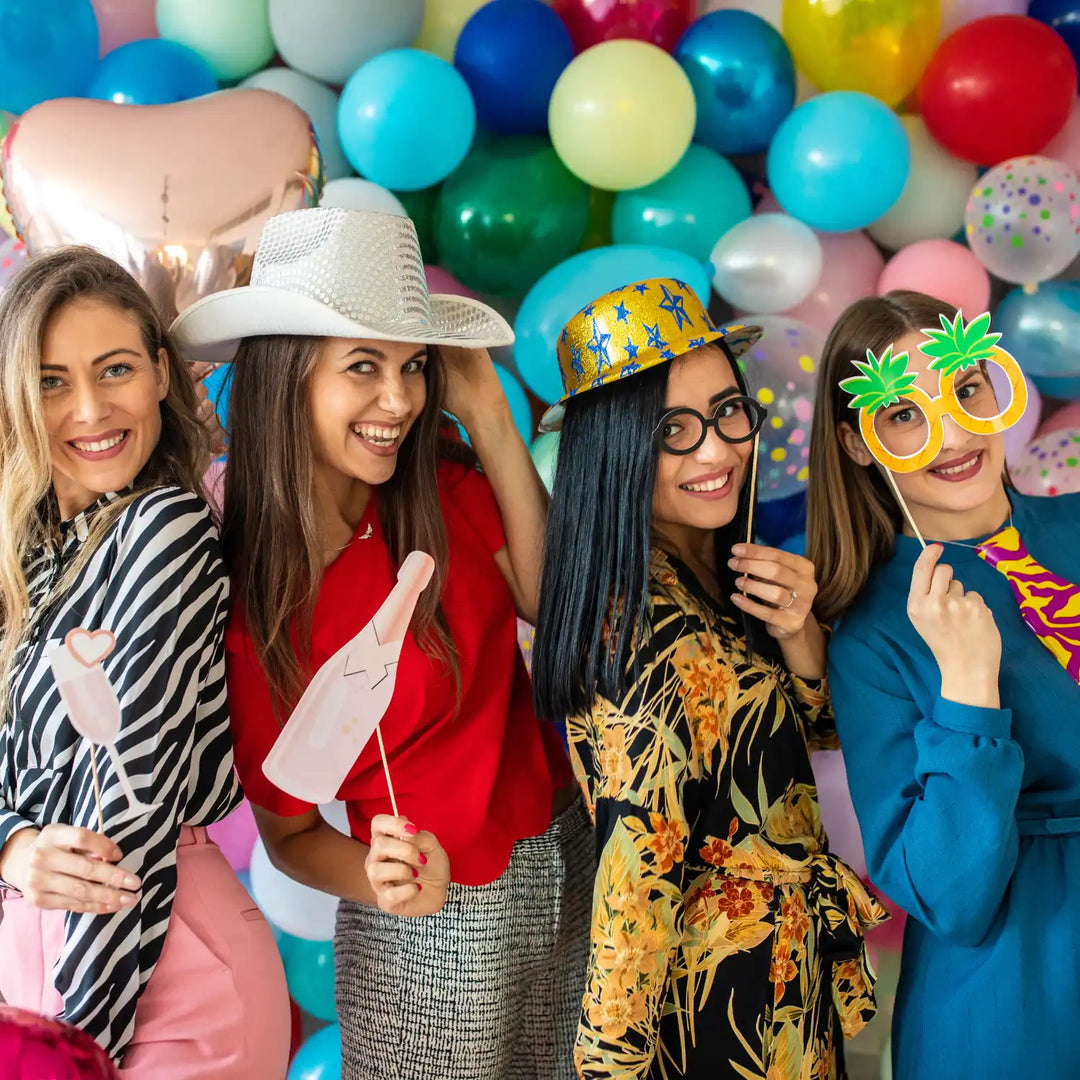 A group of friends posing with party props in front of colorful balloons