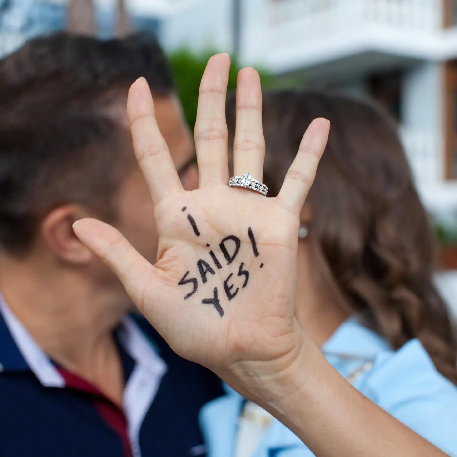 A hand with an engagement ring and ’I SAID YES!’ written on the palm.