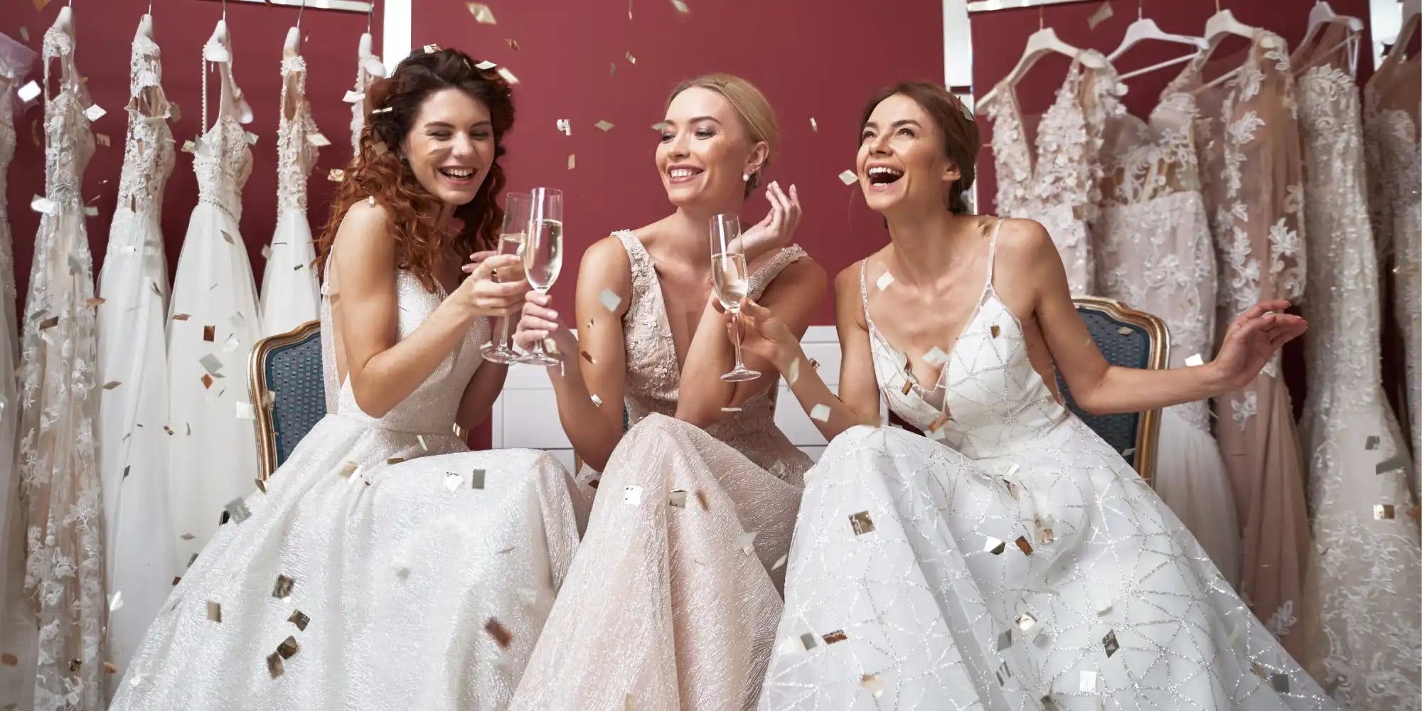 Three smiling women in white wedding dresses with confetti.